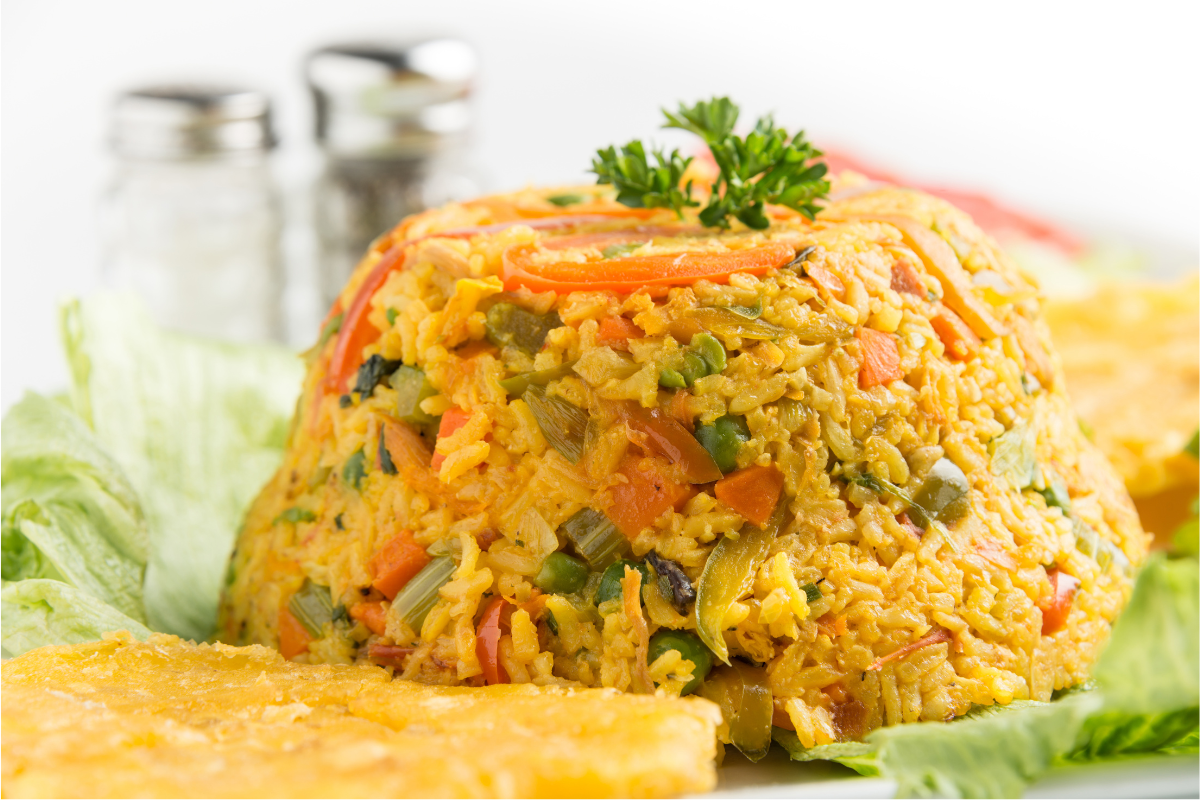 Arroz Imperial recipe featuring a vibrant layered dish of fluffy yellow rice, shredded chicken, creamy mayonnaise, peas, and red peppers, garnished with lemon wedges. Served alongside fresh ingredients.