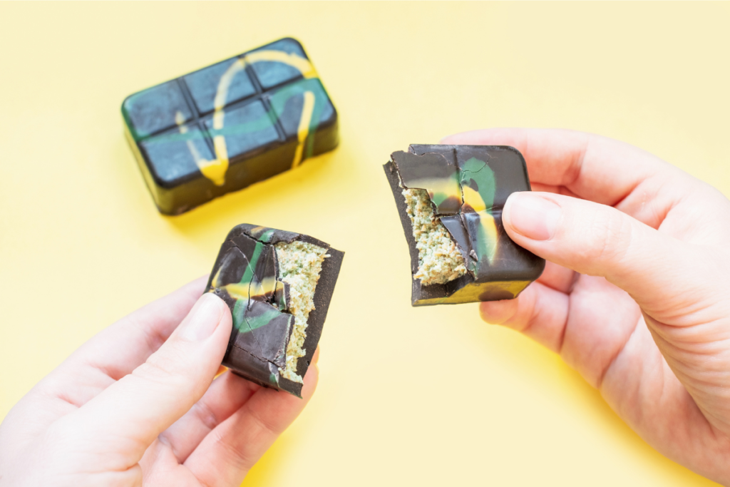 Luxurious Dubai chocolate bars with vibrant yellow and green swirls, featuring a creamy pistachio filling on a pink background