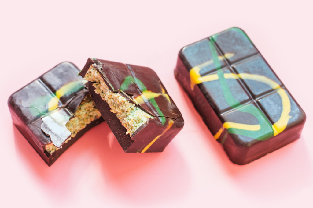 Close-up of luxurious Dubai chocolate bars with vibrant yellow and green swirls, featuring a creamy pistachio filling on a pink background.