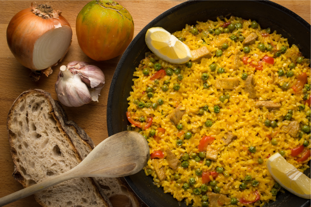 Arroz Imperial recipe featuring a vibrant layered dish of fluffy yellow rice, shredded chicken, creamy mayonnaise, peas, and red peppers, garnished with lemon wedges. Served alongside fresh ingredients like garlic, onion, and tomato, showcasing a hearty and flavorful Cuban-inspired casserole