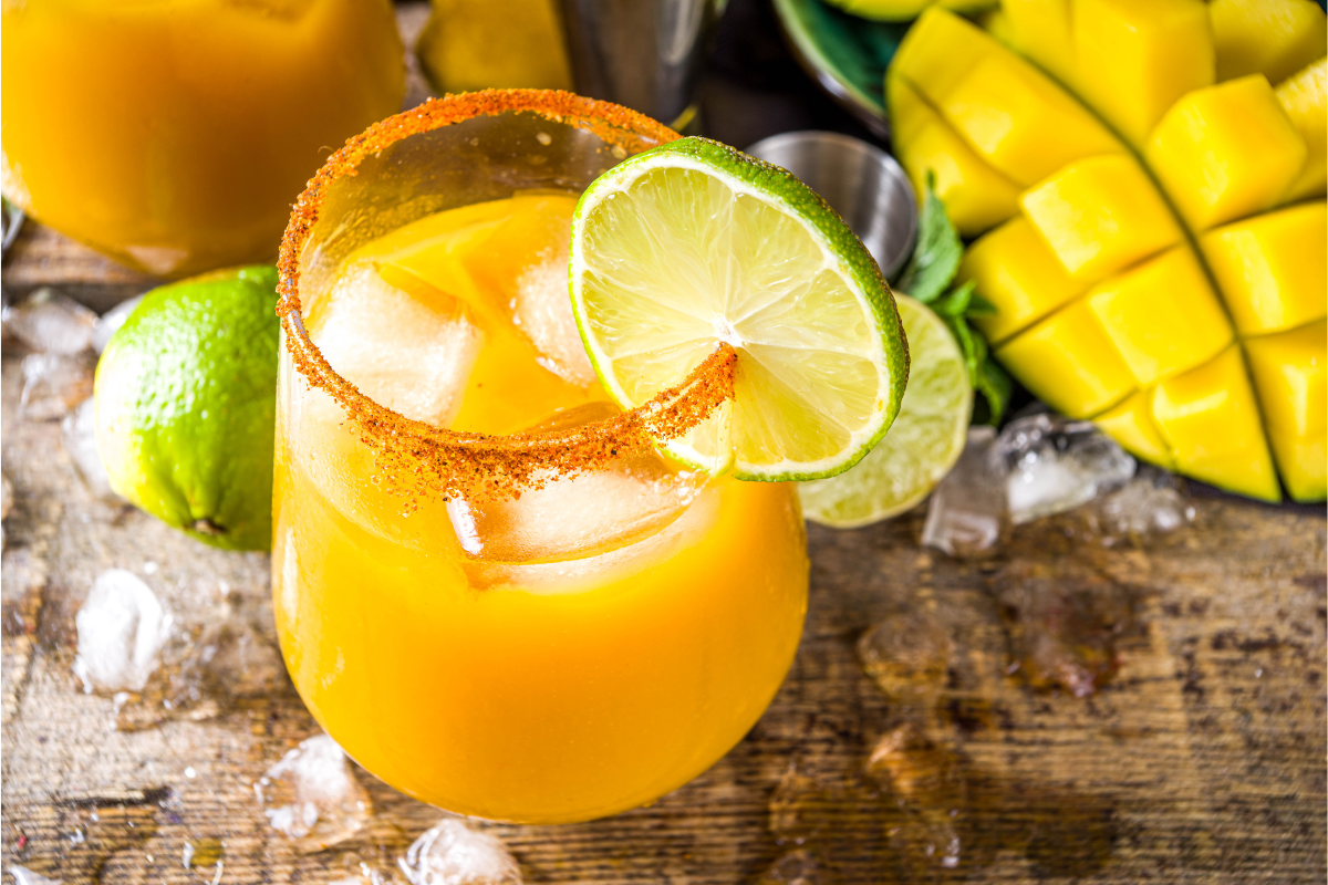 Close-up of a mango margarita with a salted rim, lime wedge, and mango slice garnish