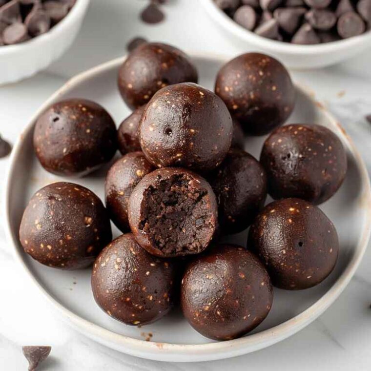 Top 10 Trending Cake Recipes of 2025 (With Gorgeous Variations) 10 A plate of glossy no-bake chocolate energy balls with chocolate chips on a white marble surface.