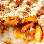 Peach Cobbler Recipe – Juicy, Buttery, and Baked to Perfection 3 Warm peach cobbler being served from a baking dish with a wooden spoon
