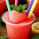 Easy Watermelon Slushies for Kids: The Ultimate Summer Cool-Down Treat 4 Three watermelon slushies with mint garnish and colorful straws, surrounded by lemon slices on a wooden surface.