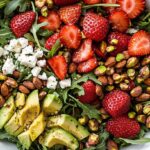 Strawberry Crunch Salad: Sweet, Crunchy & Fresh Summer Favorite 5 Fresh strawberry crunch salad with arugula, avocado, feta, toasted almonds, pistachios, and champagne vinaigrette in a white bowl.