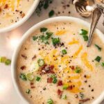 Crockpot Potato Soup: Creamy, Cheesy, and Comfort in a Bowl 5 potato soup topped with bacon, cheese, green onions, and sour cream in a scalloped bowl
