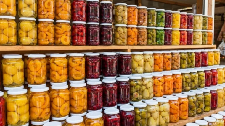 Home 16 Rows of glass jars filled with colorful home canned fruits and vegetables, including peaches, cherries, and pickles, arranged on shelves.